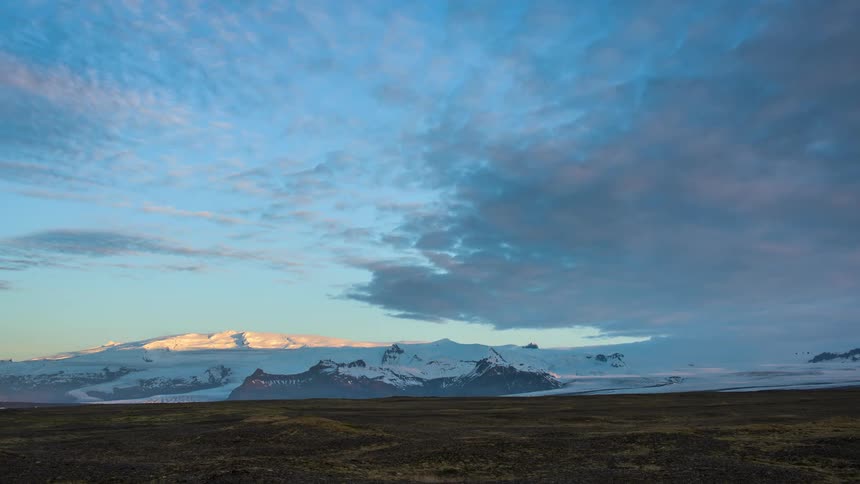 Snow covered mountains in the distance reflect the sun as clouds clear from the sky
