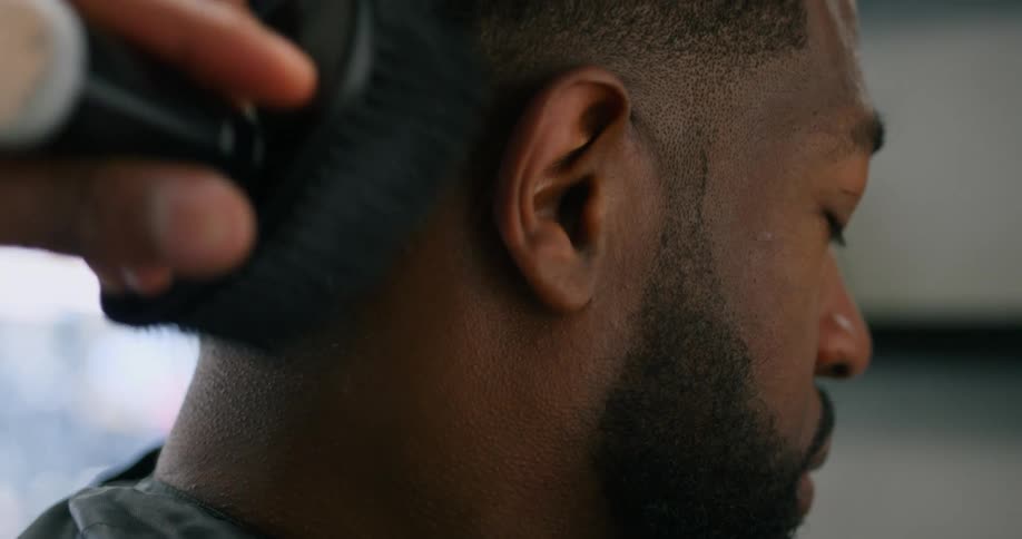 Man sits in barbers chair as barber brushes his neck and hairline