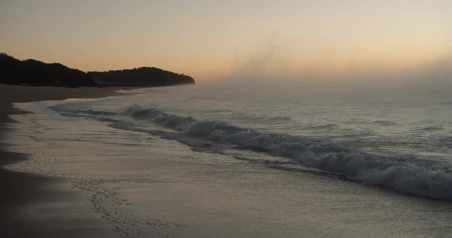 Waves roll into a sandy beach near mountains