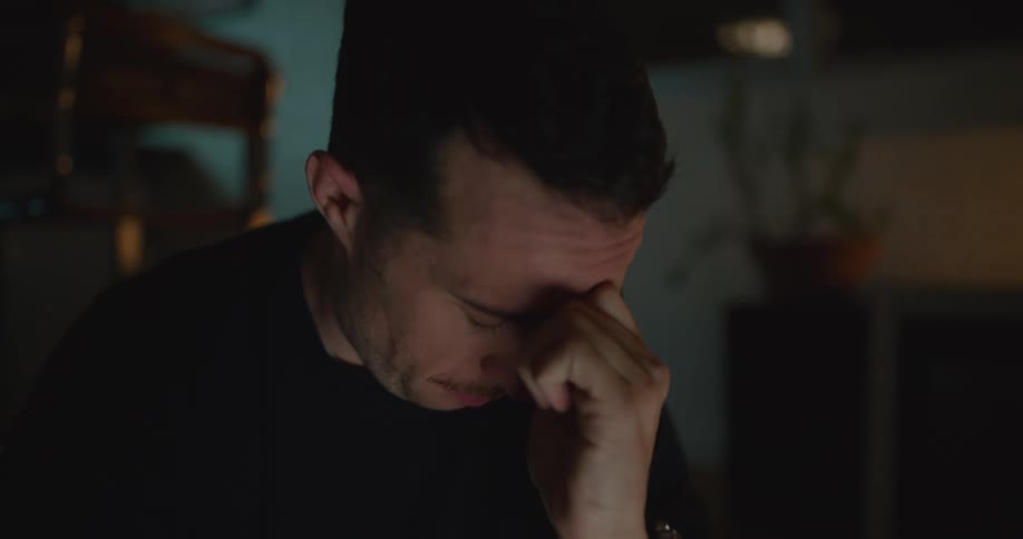 A man rubs his face and eyes tired as he works at night