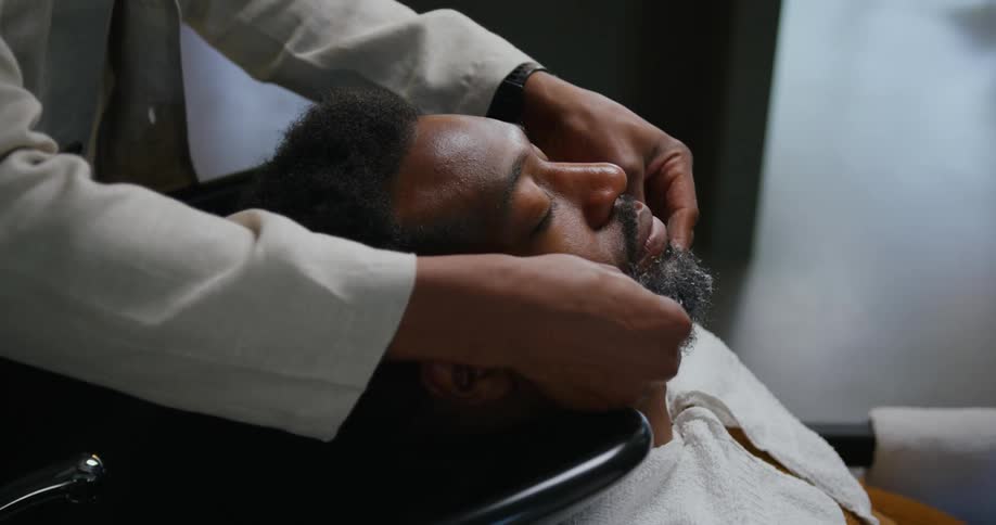 Barber with white shirt spreads foam on mans face