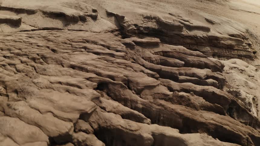 An aerial flyover of a sandy landscape reveals a canyon cut through the landscape by erosion