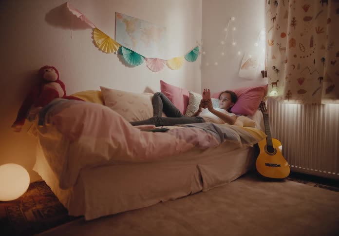 A girl scrolls through her smartphone while lying in bed