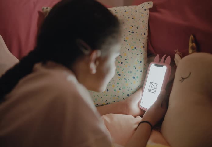 A girl smiles while looking at her phone screen lying in bed on her stomach