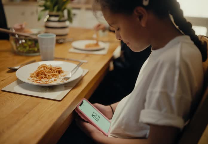 A girl picks up her phone and starts texting after eating a forkful of pasta at the dinner table dad does the same