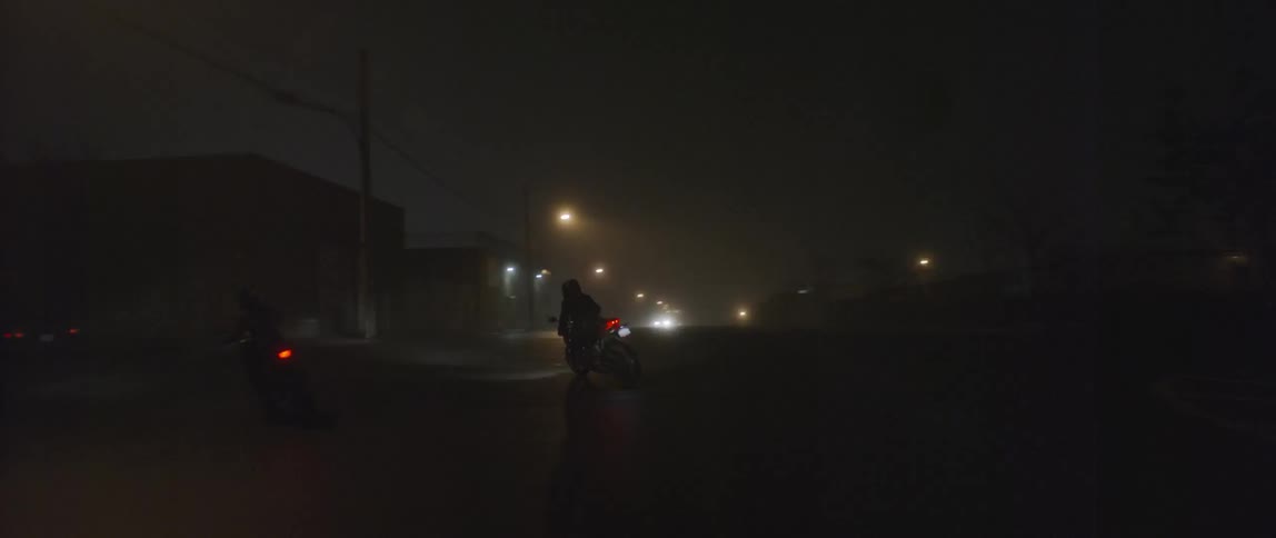 Two motorcycles follow a car at night