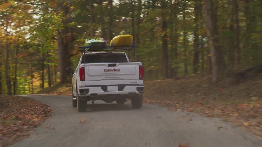 A white truck is traveling on a forest road and the sun is shining brightly through trees in fall colors