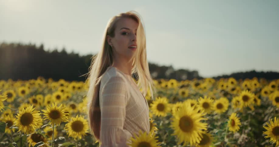 A woman with long blonde hair smiling while walking through a field of sunflowers