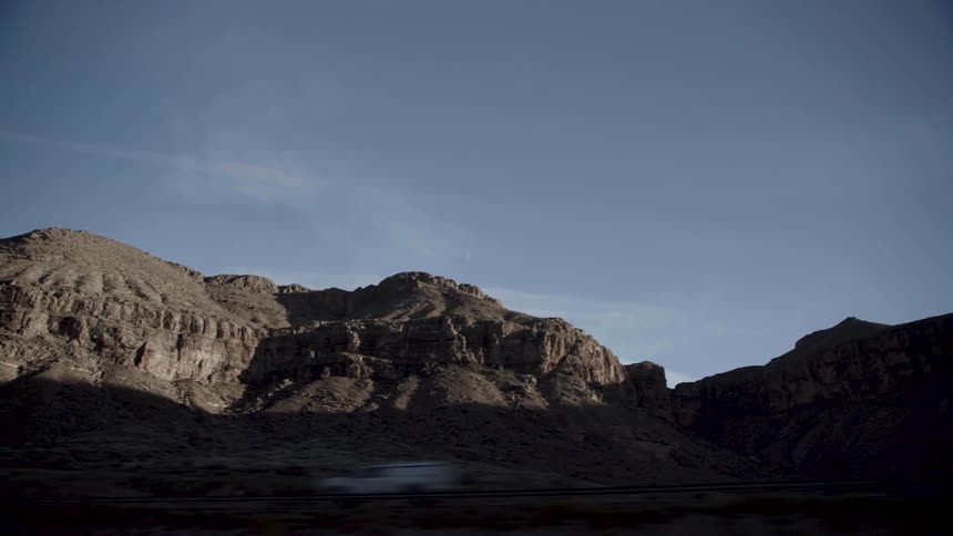 A low barren mountain ridge near a road in an arid countryside during the day