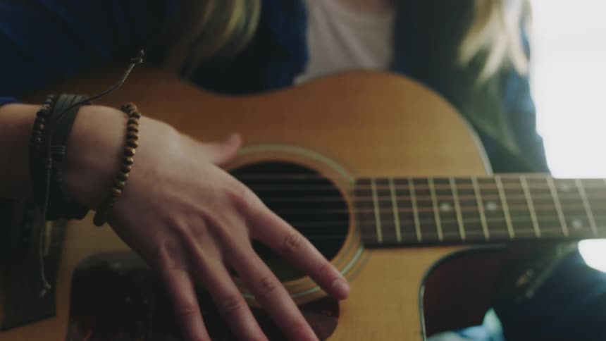 A teenage girl sitting strumming a guitar lost in thought