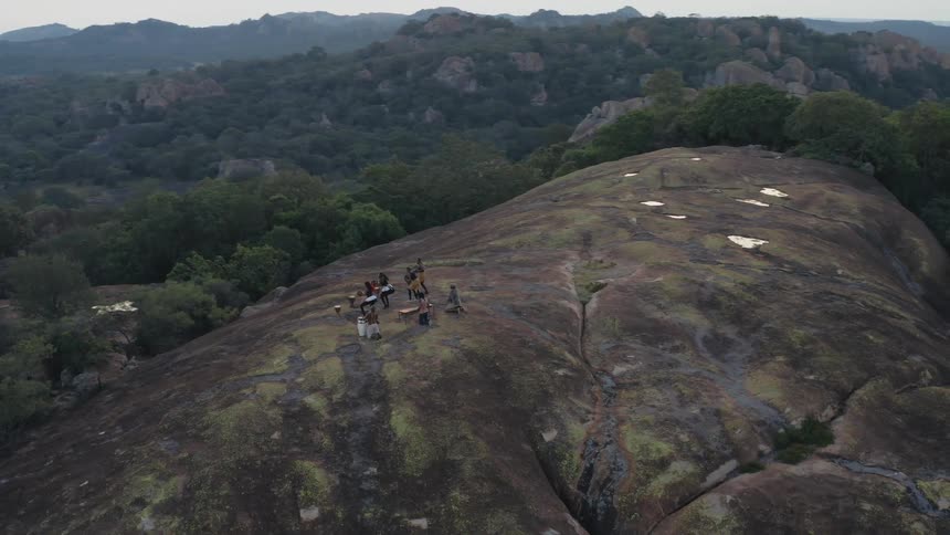 A small group of people are on a mountain top playing drums and dancing in Africa
