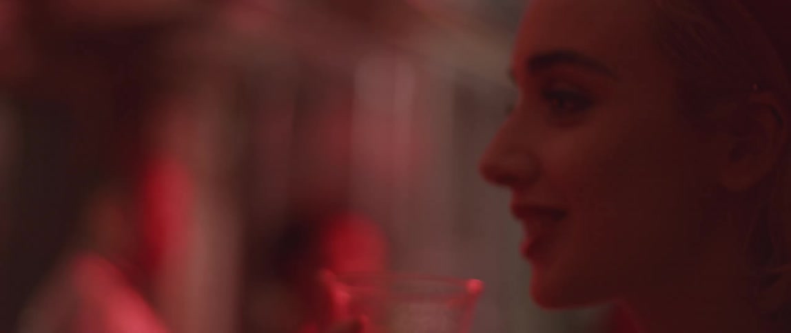 A woman drinks from a small glass while talking