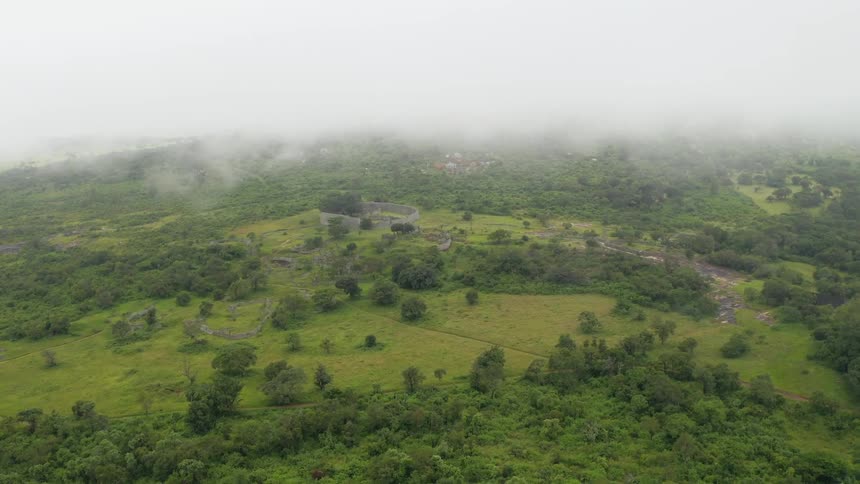 Aerial view of low white clouds over lush landscape and ruins