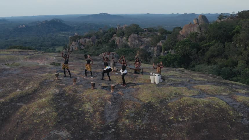 An aerial view of a group of people playing musical instruments and dancing on a hilltop