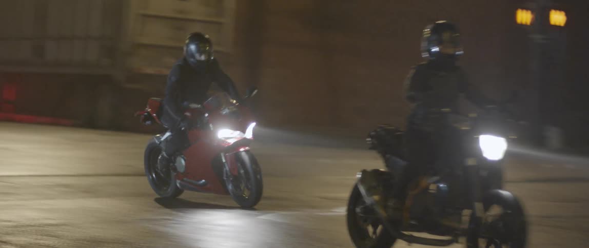 Two motorcyclists travelling along a city street at night