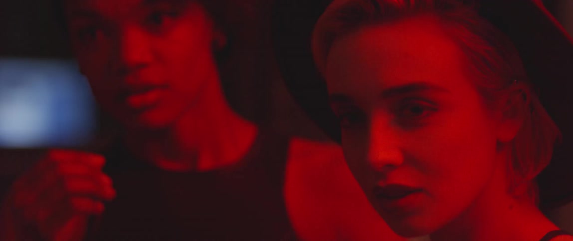 Two women are talking in a red lit room