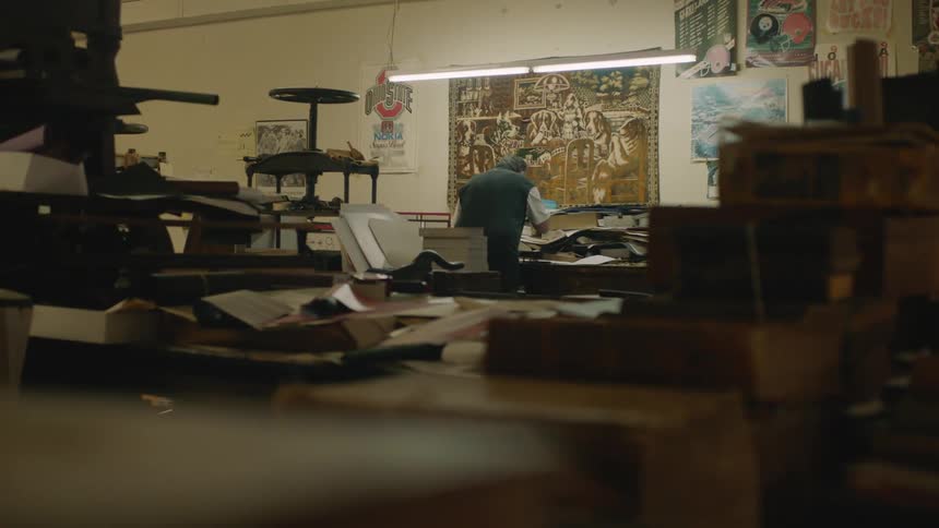 A man standing at a table in a workshop decorated with posters about music