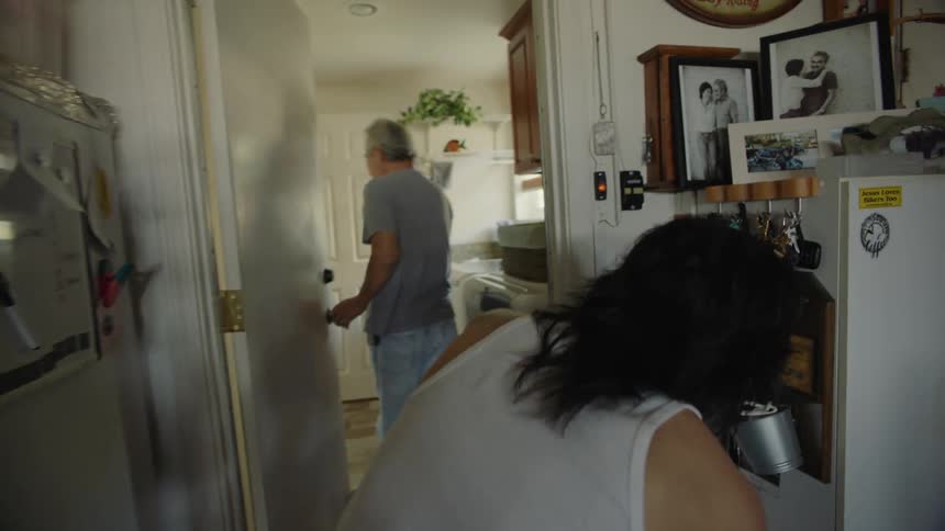 A pair of men walk through a narrow corridor in a house during the day