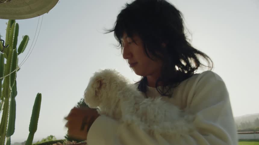A young asian man is standing outside holding his small white poodle