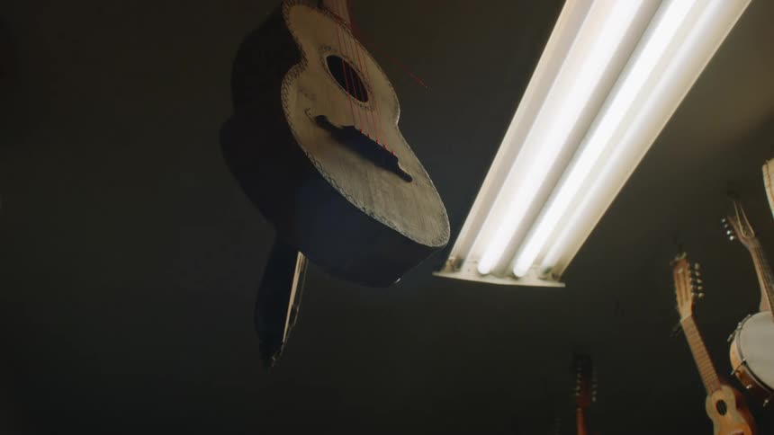 An acoustic guitar is hanging near a light and turning and there are other stringed instruments hanging in the room