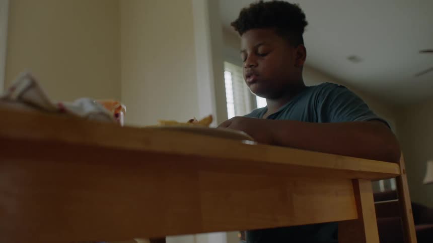 Father and son sit at dining table eating fried chicken