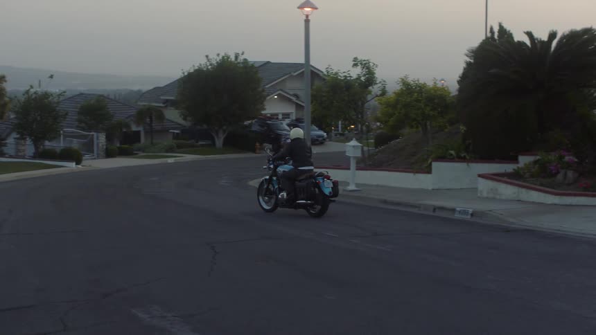 Motorcyclists drive onto sloping street as haze covers horizon