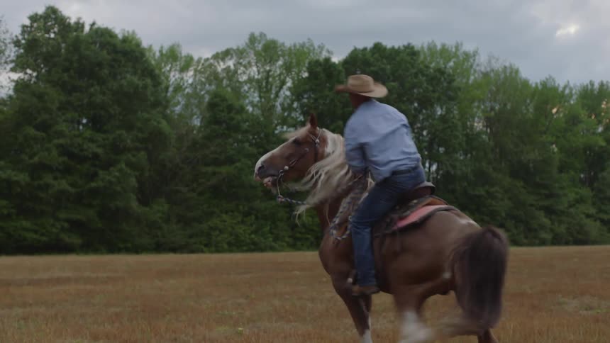 A cowboy climbs onto a spirited horse that rears up as he gets in the saddle