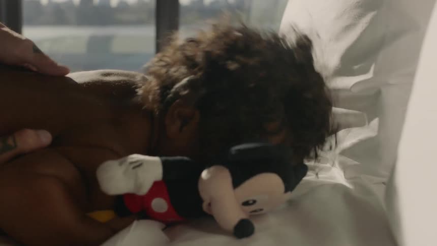 A small child is lying on a bed with his mickey mouse laughing as his father tickles him