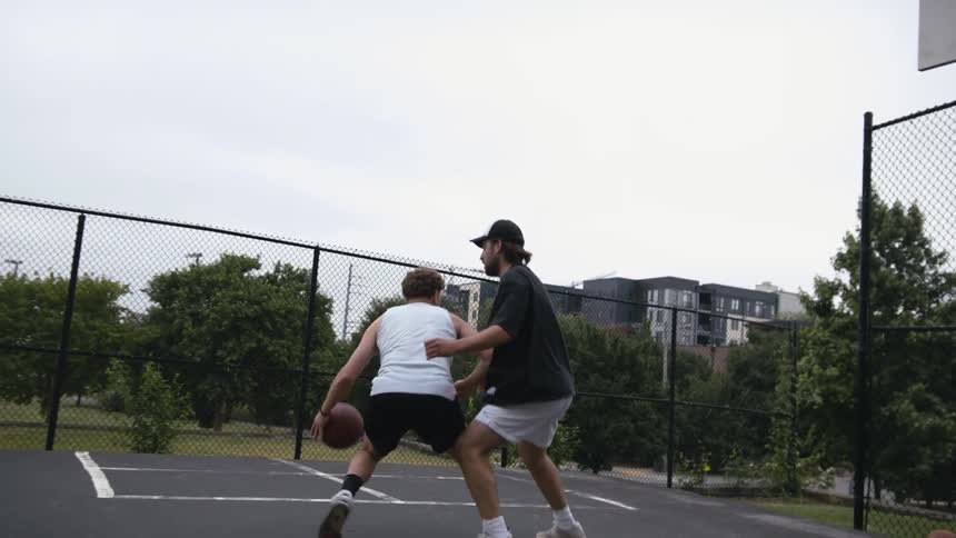 A man shoots a jump shot over his friend while playing basketball at an outdoor court