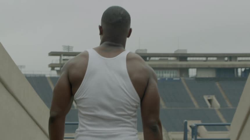 Black man in white sleeveless shirt walks into empty stadium