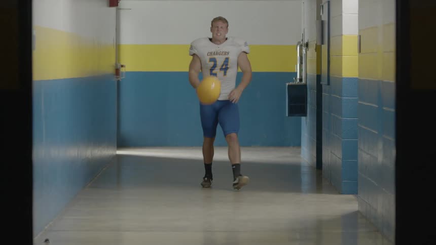 A football player walks down a hall and slams his helmet on the floor in anger