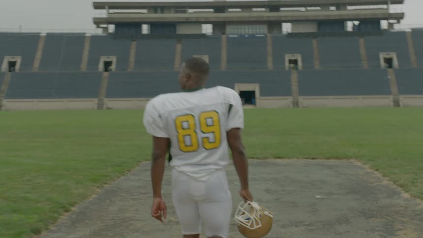 Man holding a football helmet walking into a stadium