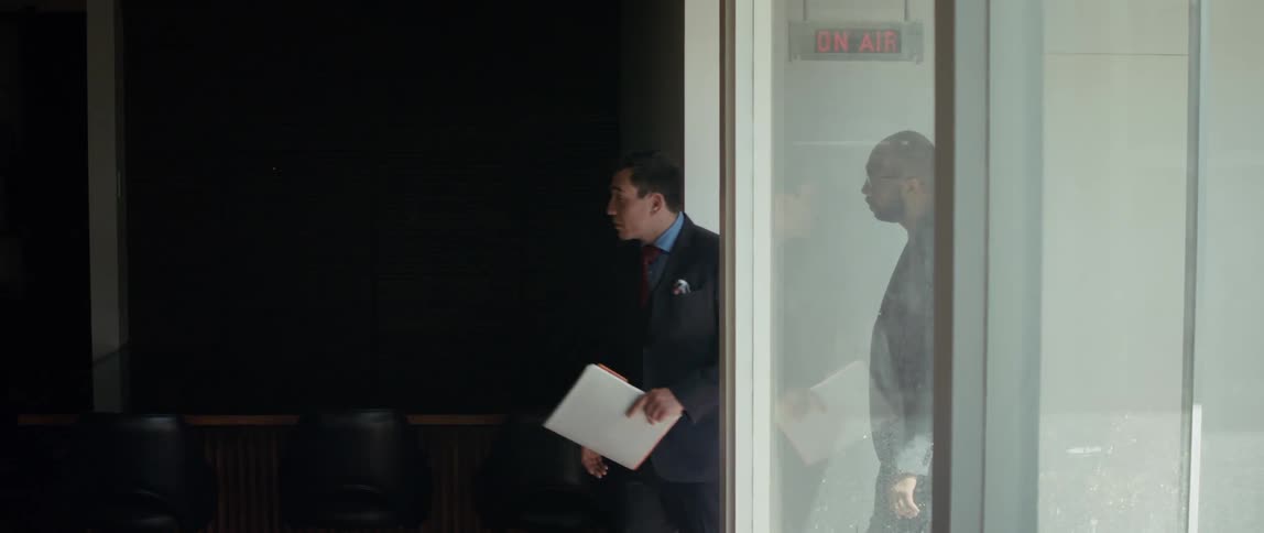A realtor talks and points as he shows a client a studio space with an on air sign outside