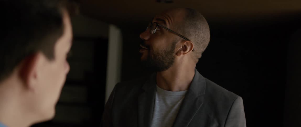 Two men are talking and one man smiles and nods his head as he looks around the room