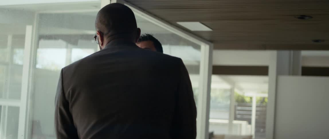 Two men in a house look out a window as they talk