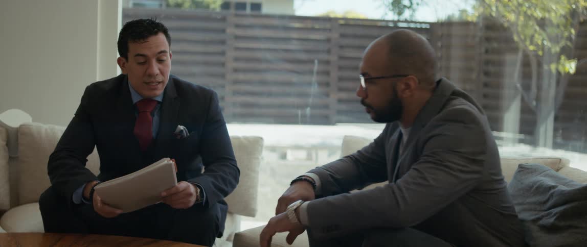 A man takes a seat on a couch listening as a realtor talks with him about the property