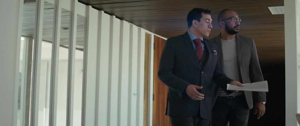 Two men talk as they walk through an office