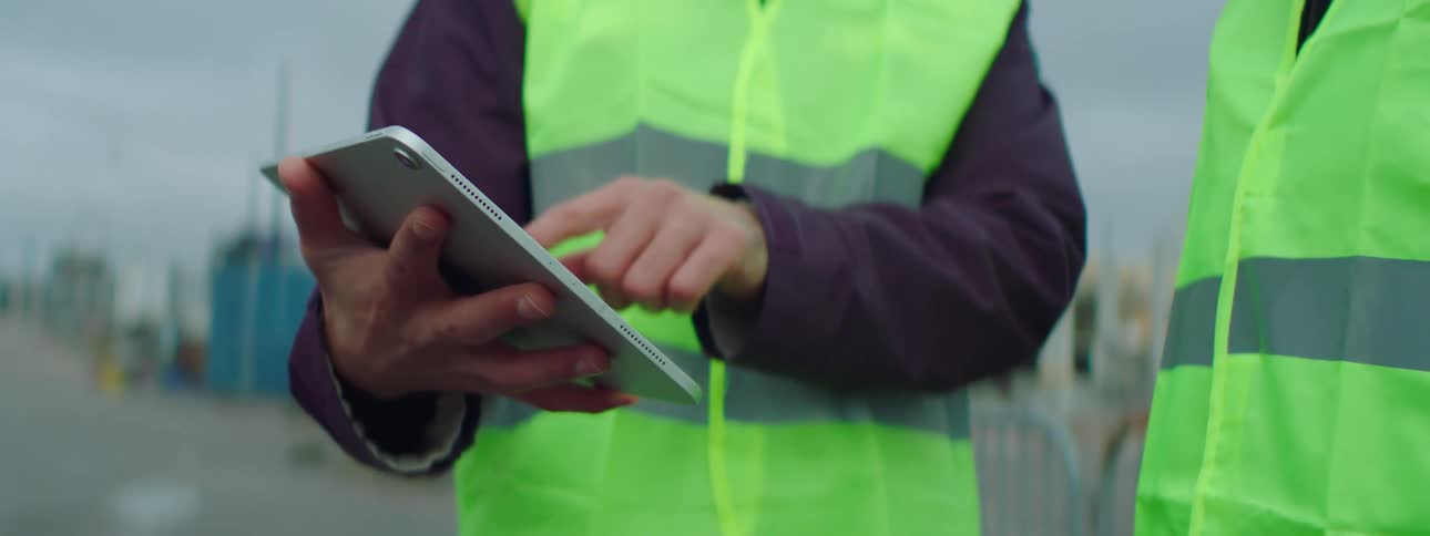 A construction worker is holding a tablet computer and showing something to another worker