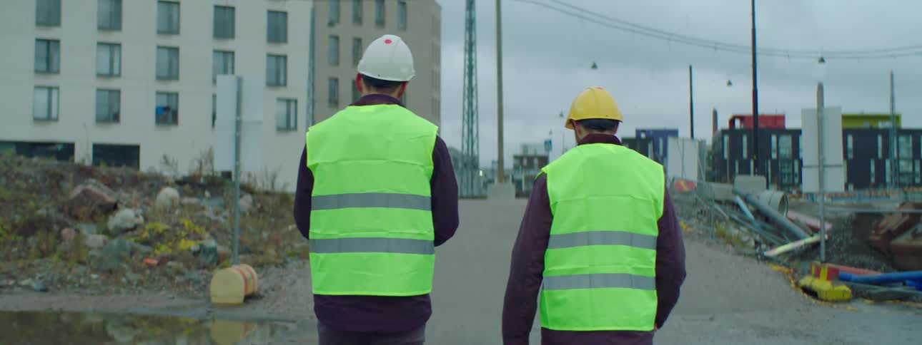 Two construction workers are walking on a sidewalk and talking