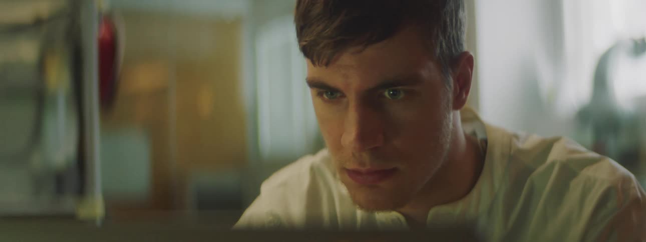 Man leans forward to study computer screen in maker lab with window behind him