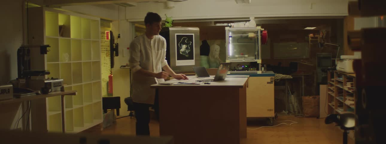 Man uses a laptop that is sitting on a counter top then walks off to the right of the counter top and wipes his hands together