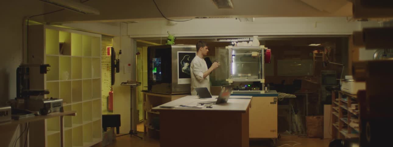 A lab worker checks on a three dimensional printer before sitting down to work on his laptop