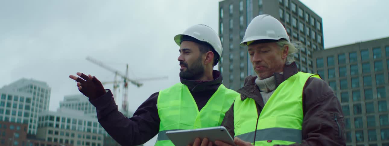 Construction workers on a site discuss plans using a tablet