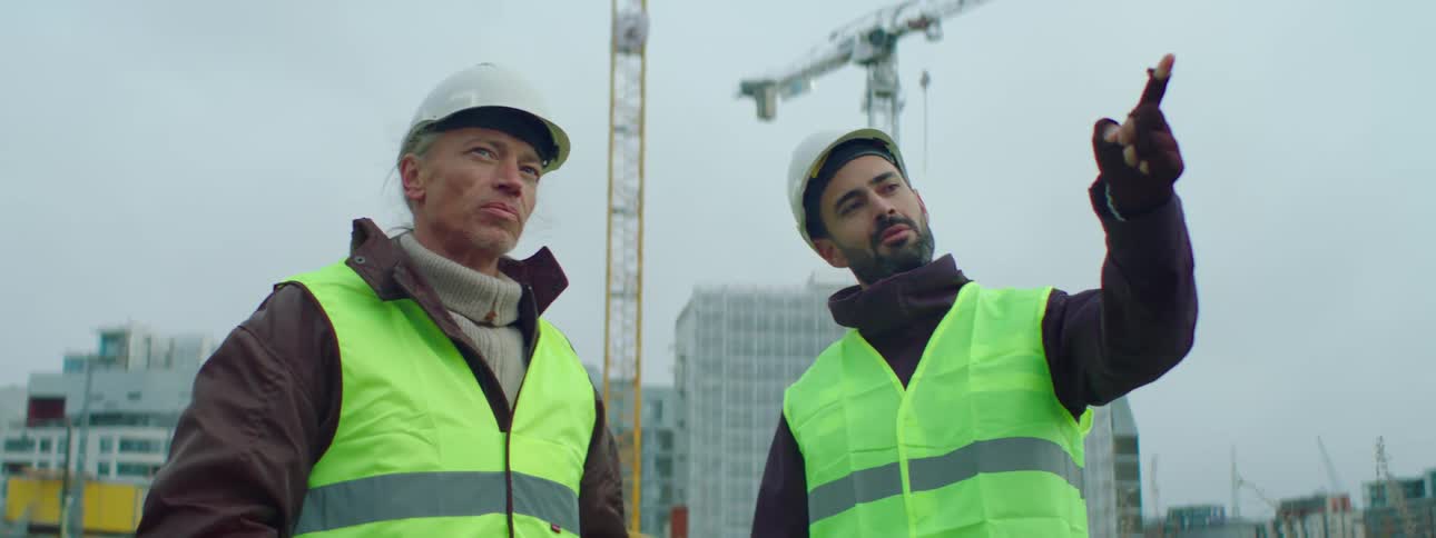 Two construction workers talk together outside at a job site