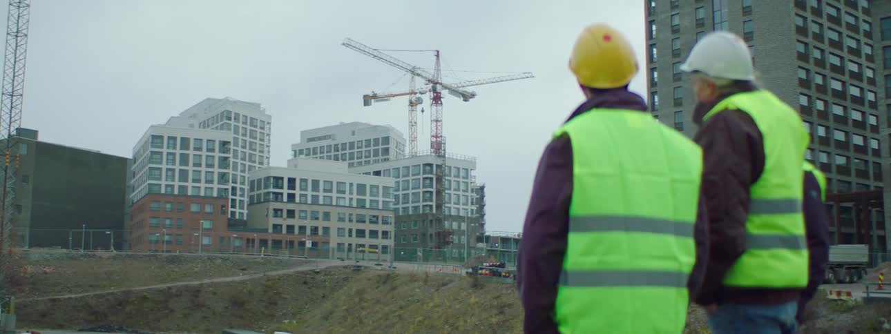Two male construction workers standing at the construction site wearing safety helmets and vests