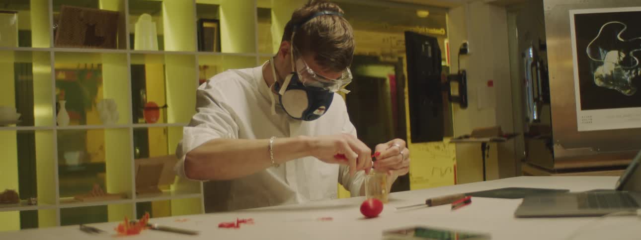 Man wearing a mask and goggles squeezes something into a clear cup