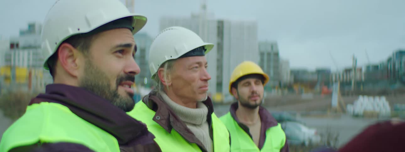 Three construction workers stand together as one talks and points at a site
