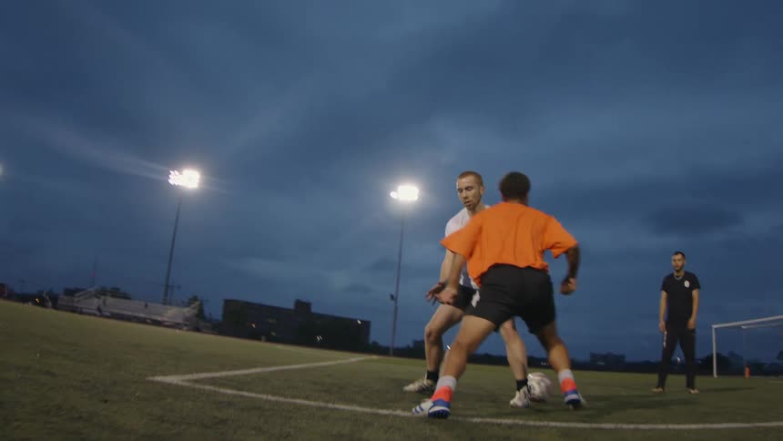 Men play soccer on sports field under stadium lights at night
