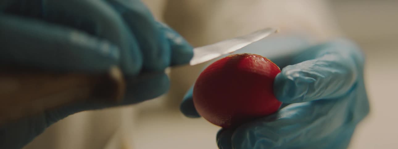 Person wearing gloves uses knife to shave small hairs from a piece of fruit