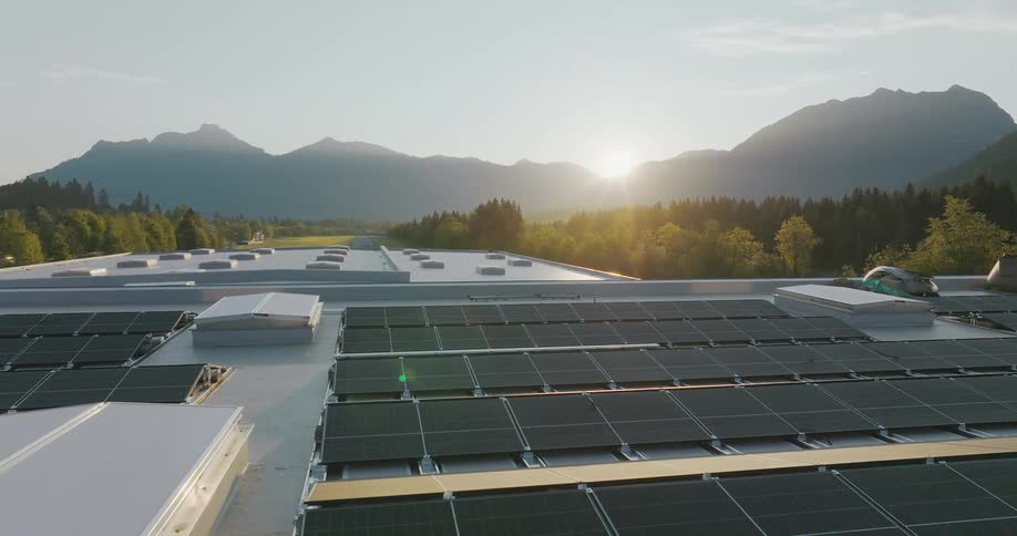The sun shines brightly over mountains onto solar panels on the roof of a building
